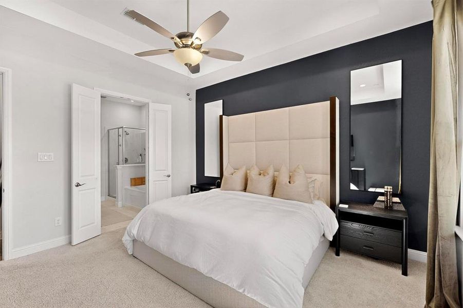 Bedroom with light colored carpet, a ceiling fan, connected bathroom, and a tray ceiling Bedroom with light colored carpet, a ceiling fan, connected bathroom, and a tray ceiling