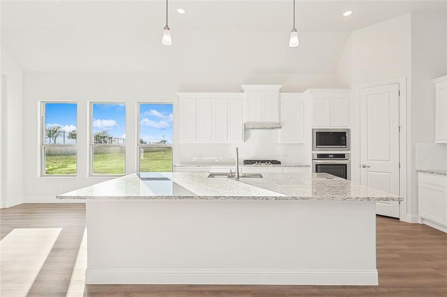 Kitchen with white cabinets, light stone countertops, dark wood finished floors, a center island with sink, and lofted ceiling Kitchen with white cabinets, light stone countertops, dark wood finished floors, a center island with sink, and lofted ceiling