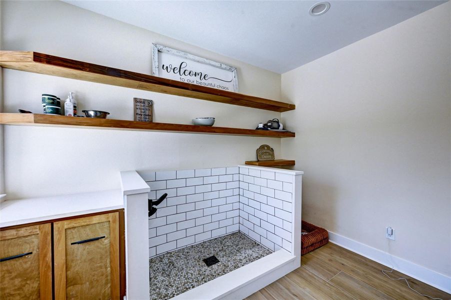 This room features a stylish pet washing station with white subway tiles and a pebble floor. Wooden shelves provide ample storage, and there's a cozy dog bed in the corner. Perfect for pet owners.