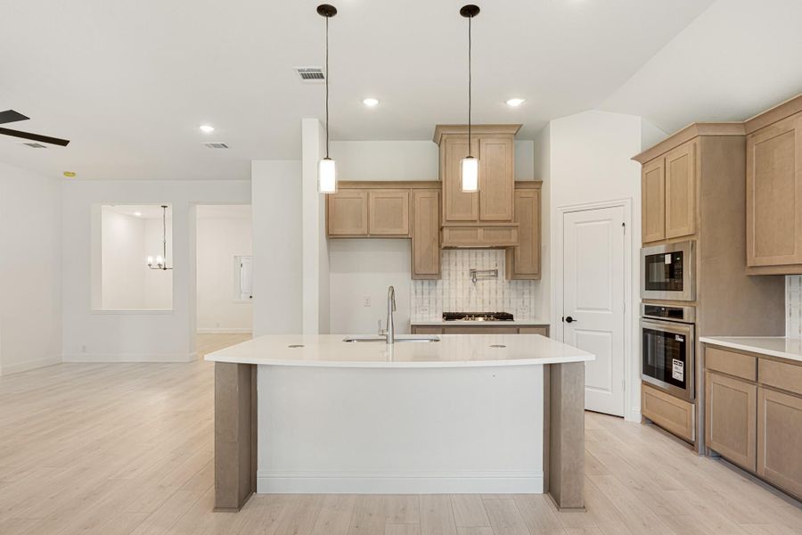 Kitchen with large center island, light wood cabinets, pendant lights, and stainless steel double ovens