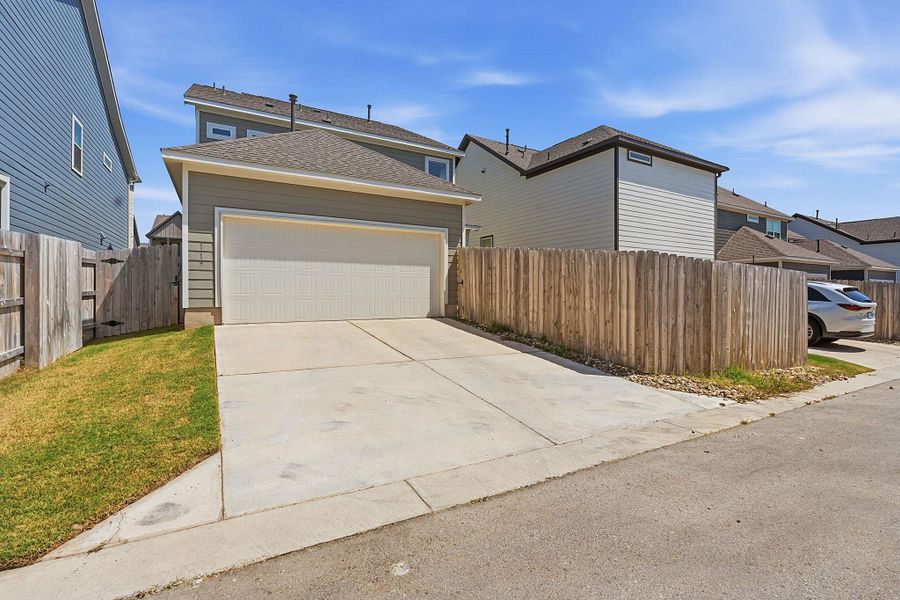 Concrete driveway leads to an attached garage with a modern overhead door, flanked by well-maintained fencing. Concrete driveway leads to an attached garage with a modern overhead door, flanked by well-maintained fencing.