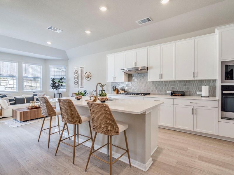 A sleek island kitchen featuring crisp white cabinetry and bright recessed lighting flows into a well-lit living area.