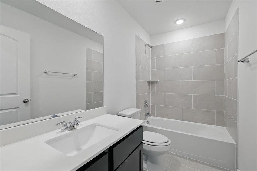Full bath with tile patterned floors, toilet, vanity, and washtub / shower combination Full bath with tile patterned floors, toilet, vanity, and washtub / shower combination