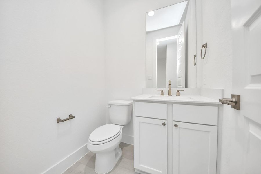 Sophisticated half bathroom adorned with contemporary finishes. The elegant 5-panel door welcomes you to a space where style meets functionality. Notice the sleek hardware accents that add a touch of modern charm. The vanity boasts light-colored countertops, beautifully complemented by a tasteful vanity light, creating a well-lit and inviting atmosphere.