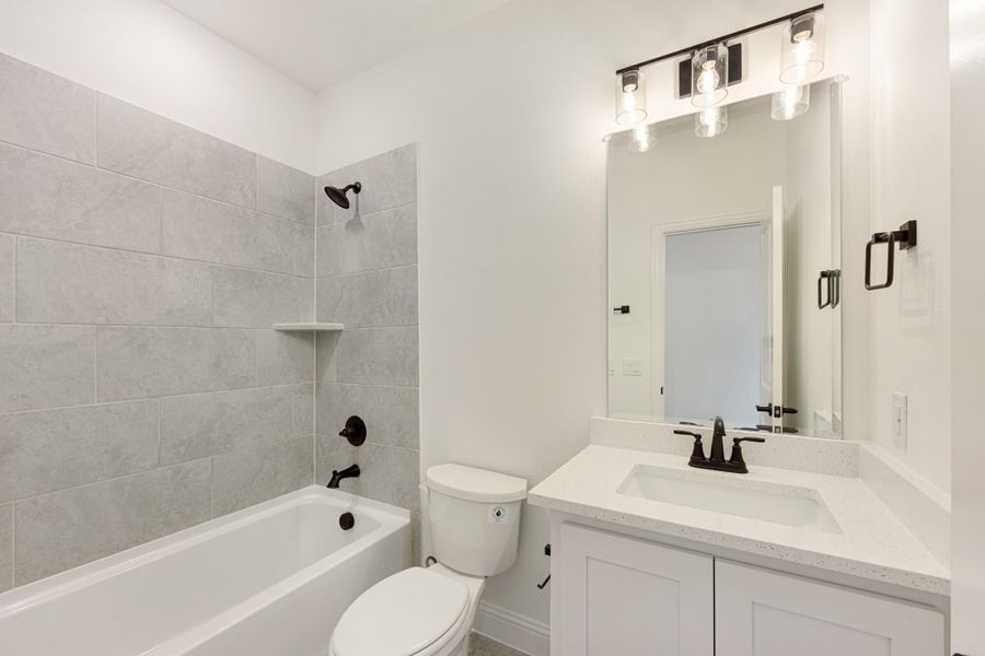 Bathroom with tub-shower combo, gray tile surround, white vanity with quartz countertop, and black fixtures