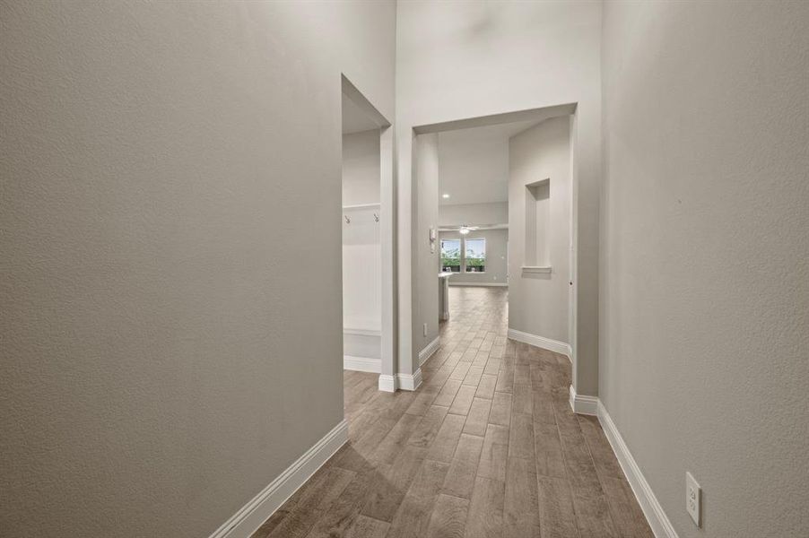 Long hallway entry leading into the open-concept living space, featuring wood-look tile floors and high ceilings that enhance the flow of the home.