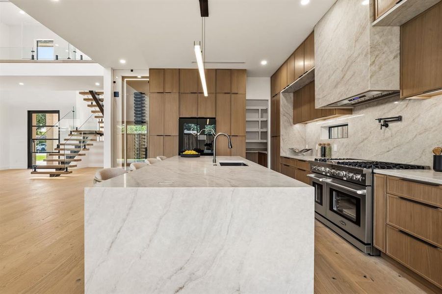 White stone waterfall island with integrated sink, stainless steel appliances, wood-finish cabinetry, and light wood-finish flooring