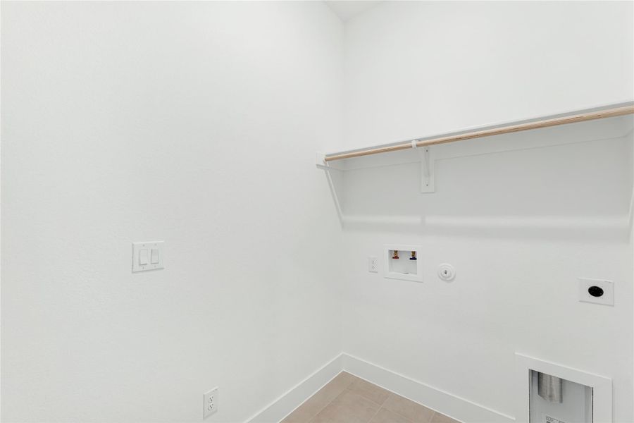Empty laundry room with washer hookups, upper shelf with hanging rod, and tile floor