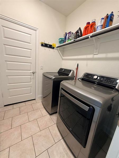 Laundry room featuring neutral-toned tile flooring, built-in shelving, and a paneled door Laundry room featuring neutral-toned tile flooring, built-in shelving, and a paneled door