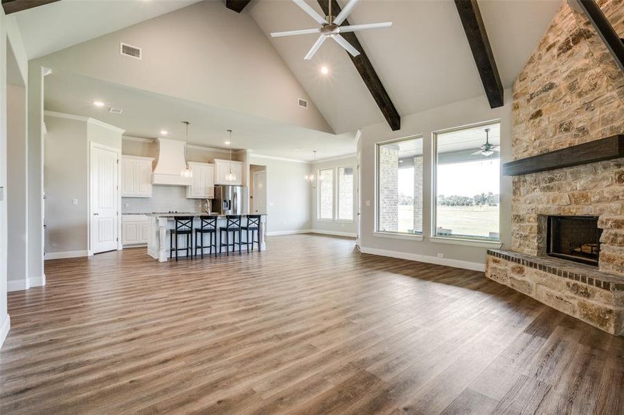 Unfurnished living room featuring beam ceiling, ceiling fan, a stone fireplace, wood-type flooring, and high vaulted ceiling