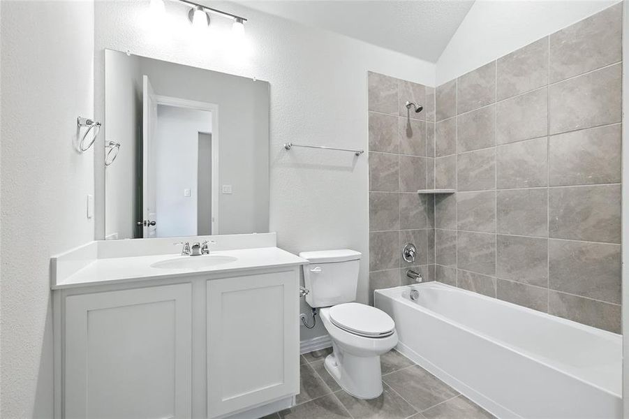 Bathroom featuring vanity, tub / shower combination, light tile patterned flooring, a textured wall, and lofted ceiling Bathroom featuring vanity, tub / shower combination, light tile patterned flooring, a textured wall, and lofted ceiling