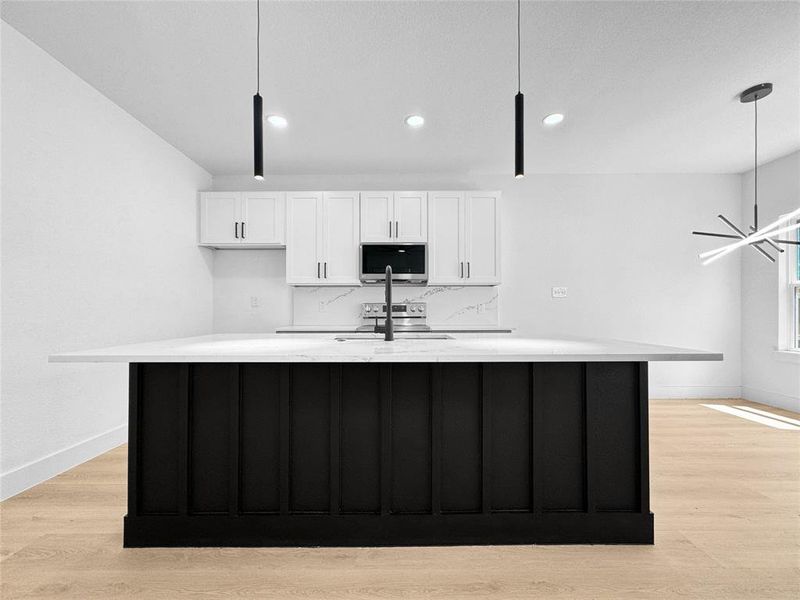 Kitchen featuring white cabinetry, light wood-type flooring, dark cabinets, a kitchen island with sink, and recessed lighting