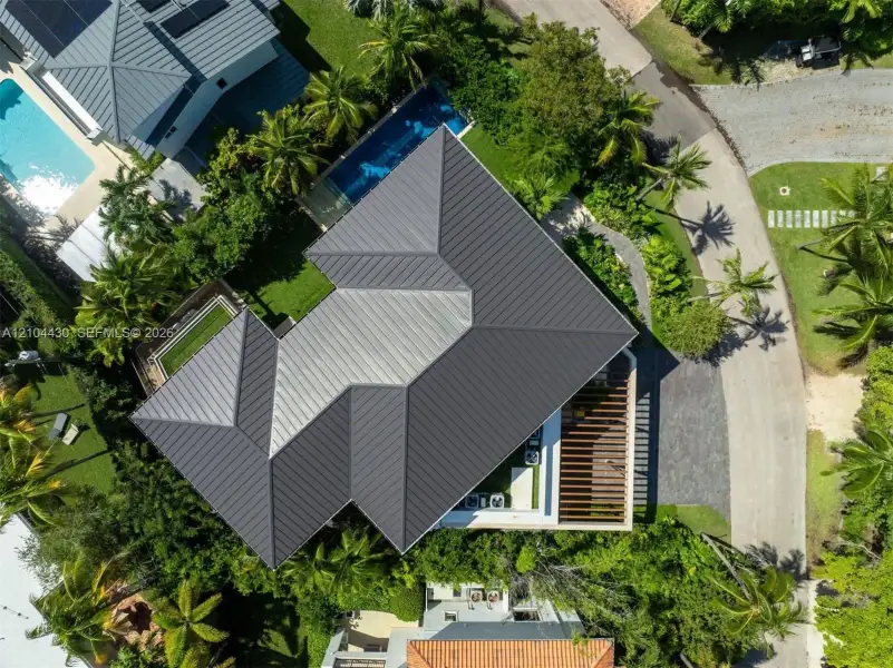 Aerial perspective featuring a metal roof, rectangular swimming pool, integrated patio pergola, and mature landscaping