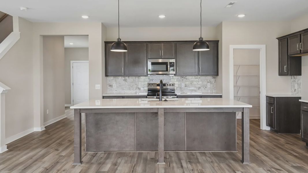 Kitchen with dark cabinetry, quartz countertops, pendant lighting, and tile backsplash Kitchen with dark cabinetry, quartz countertops, pendant lighting, and tile backsplash