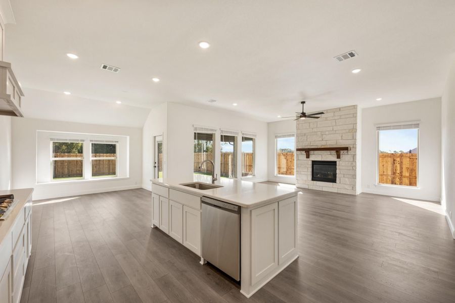 Open-concept kitchen and living area with white island, hardwood floors, and stone fireplace Open-concept kitchen and living area with white island, hardwood floors, and stone fireplace