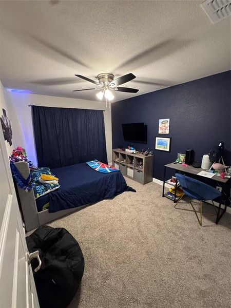 Bedroom 5 featuring a ceiling fan with integrated lighting, dark accent wall, window with dark drapes, and a desk area