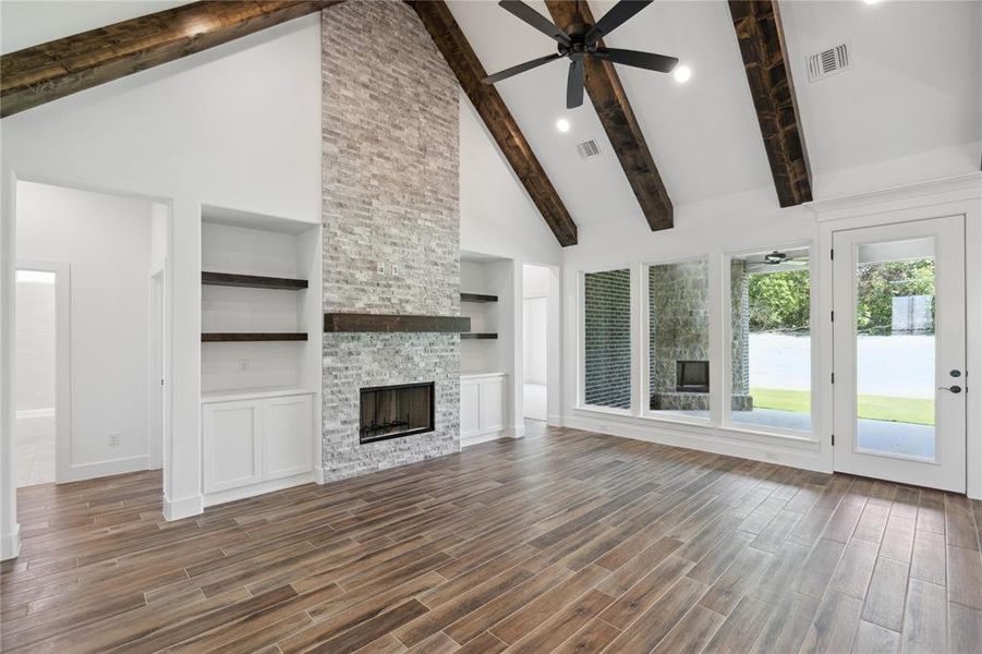 Unfurnished living room with built in features, beamed ceiling, a stone fireplace, high vaulted ceiling, and ceiling fan