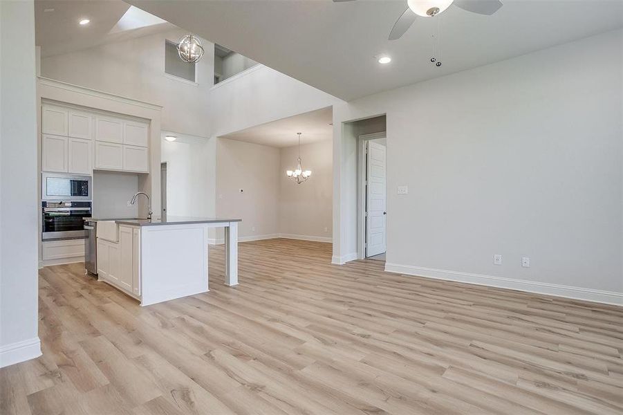 Kitchen with light hardwood / wood-style floors, ceiling fan with notable chandelier, white cabinets, and a center island with sink