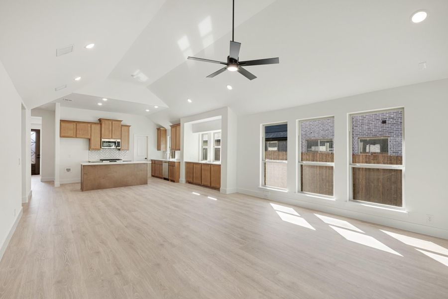 Open living area with vaulted ceiling, ceiling fan, and kitchen with wood cabinets and center island
