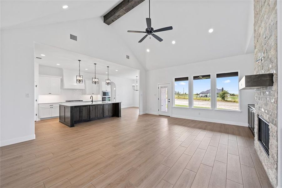 Unfurnished living room featuring a fireplace, beamed ceiling, high vaulted ceiling, ceiling fan, and light wood finished floors