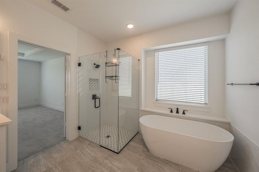 Primary bathroom features a freestanding soaking tub, a glass-enclosed shower with black fixtures, and tiled flooring