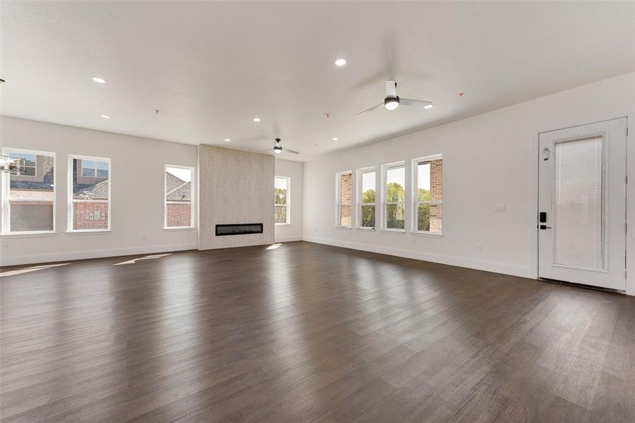 Unfurnished living room featuring dark wood-type flooring, a large fireplace, and ceiling fan