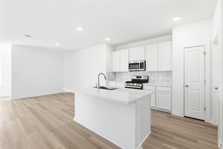Kitchen with appliances with stainless steel finishes, an island with sink, white cabinets, light wood finished floors, and tasteful backsplash