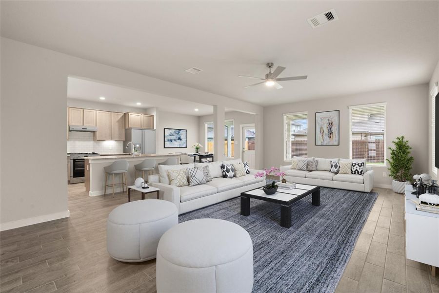 This photo showcases a spacious, open-concept living area with modern decor. The room features a comfortable seating arrangement, a large area rug, and ample natural light from multiple windows. The adjacent kitchen includes a breakfast bar with stylish stools, creating a seamless flow between spaces.