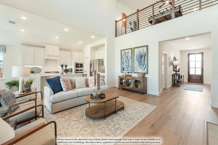 Open-concept living room with two-story ceiling, hardwood floors, and kitchen visible in background