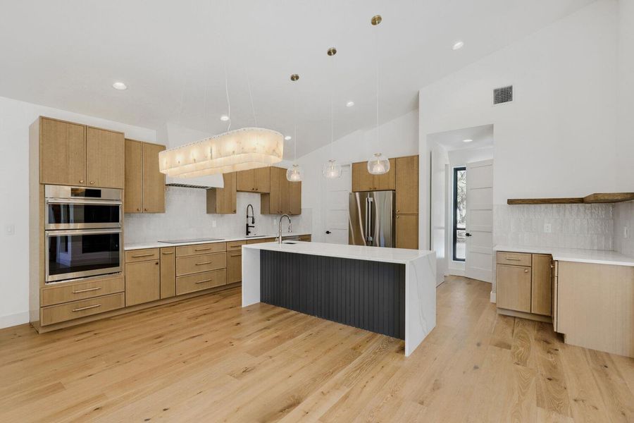 Two tone kitchen featuring backsplash, light stone counters, stainless steel appliances, a center island with sink, and light wood-style floors Two tone kitchen featuring backsplash, light stone counters, stainless steel appliances, a center island with sink, and light wood-style floors