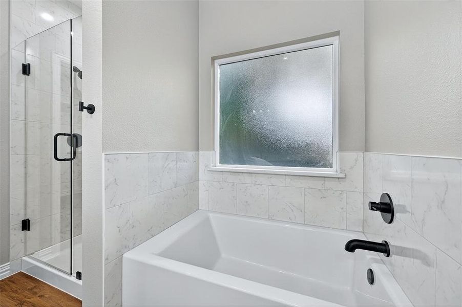 Bathroom featuring a garden tub, a stall shower, and a textured wall Bathroom featuring a garden tub, a stall shower, and a textured wall