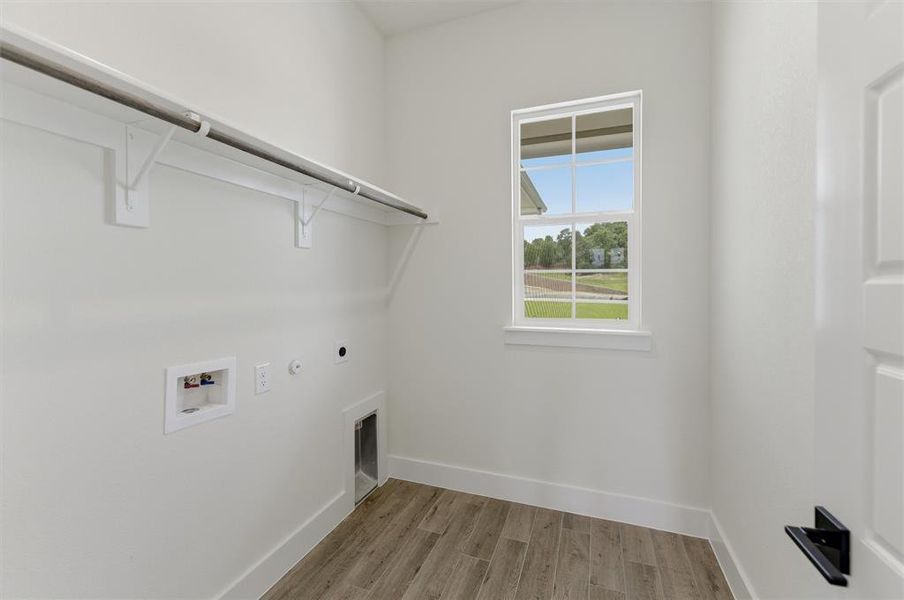 Dedicated laundry room featuring wood-finish flooring, a multipane window, and a built-in hanging rod with shelving