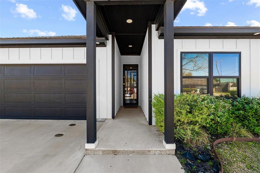 Doorway to property featuring an attached garage, board and batten siding, and concrete driveway