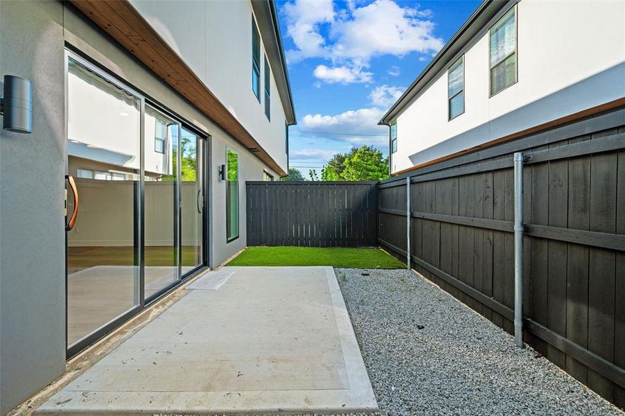 Backyard features a concrete patio accessible through sliding glass doors. Turf yard is accented by a decorative gravel border. Wood privacy fencing encloses the outdoor space.