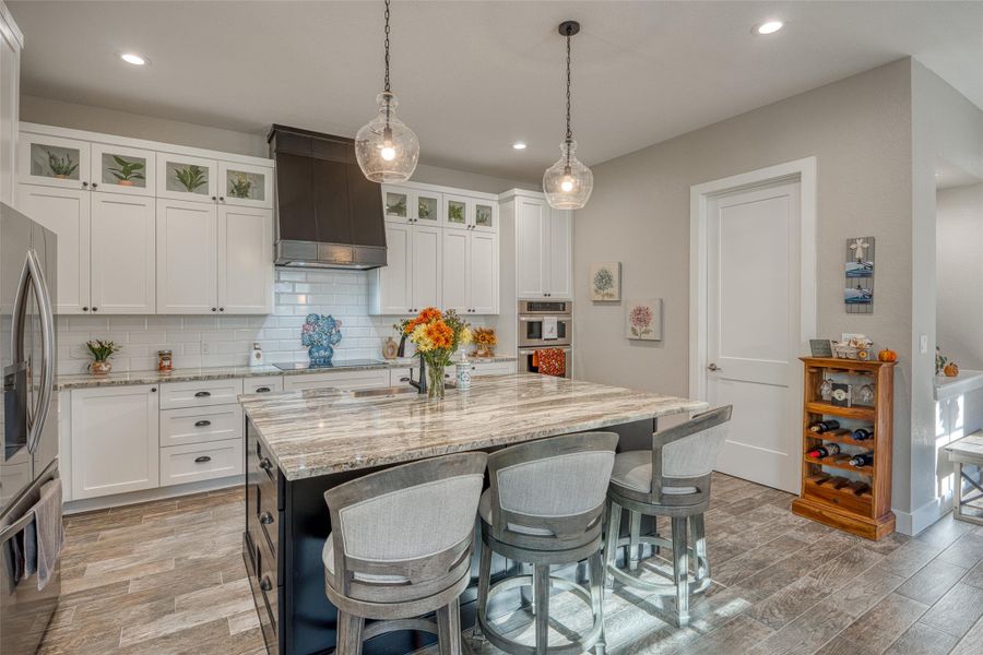 Kitchen featuring white cabinets, a kitchen bar, decorative backsplash, light stone countertops, and custom range hood