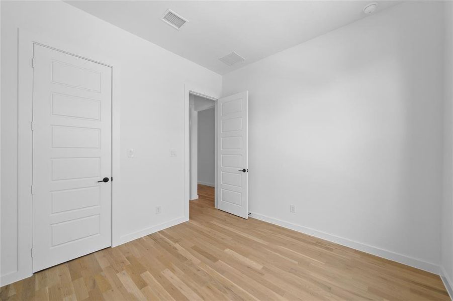 Bright interior room featuring light wood-finish flooring, white baseboards, and a contemporary five-panel door with matte black hardware