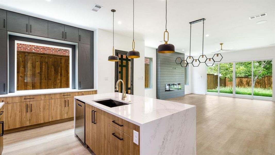 Kitchen with a kitchen island with sink, sink, ceiling fan, decorative light fixtures, and light stone counters