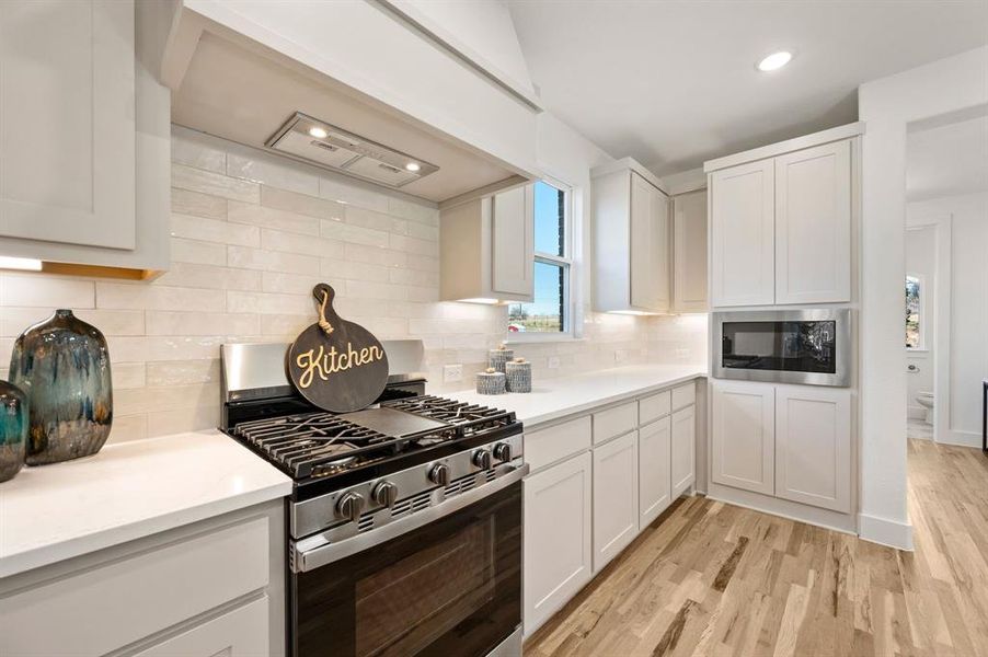 Kitchen featuring stainless steel appliances, light wood-type flooring, white cabinets, recessed lighting, and tasteful backsplash