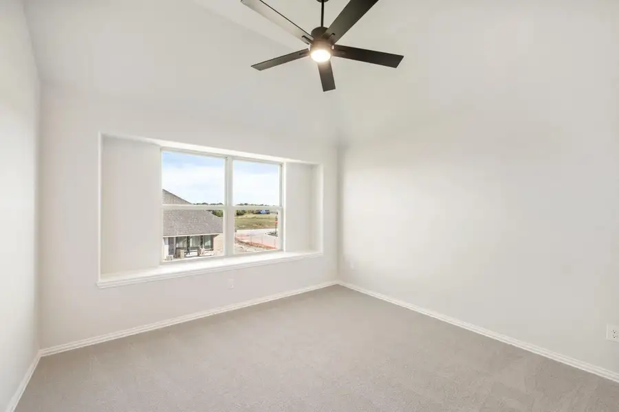 Empty bedroom with carpet flooring, ceiling fan, and large window overlooking neighborhood