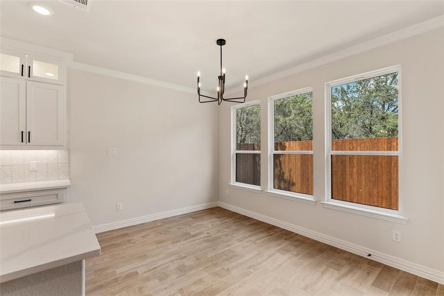 Unfurnished dining area featuring crown molding, light hardwood / wood-style flooring, and a notable chandelier