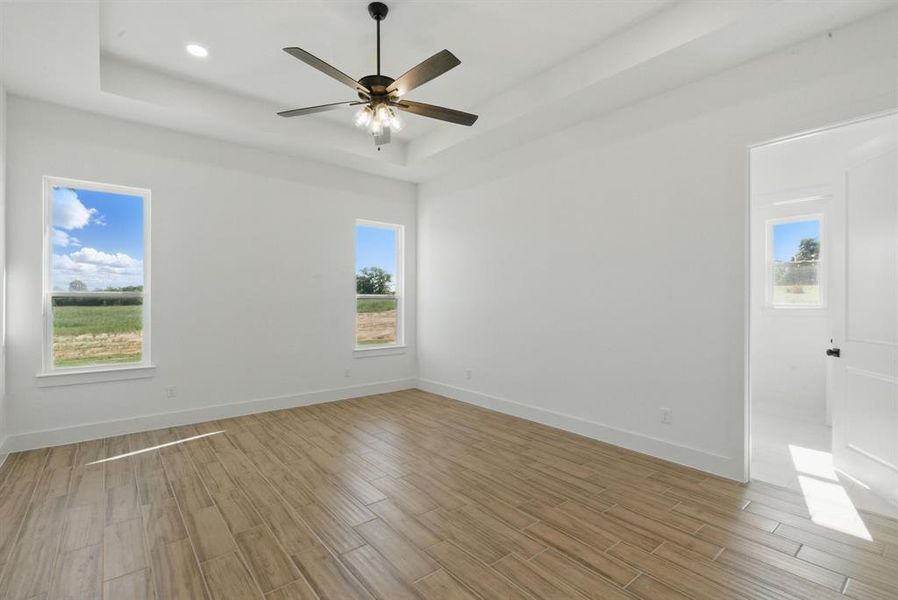 Unfurnished room with a raised ceiling, light wood-style flooring, and a ceiling fan Unfurnished room with a raised ceiling, light wood-style flooring, and a ceiling fan