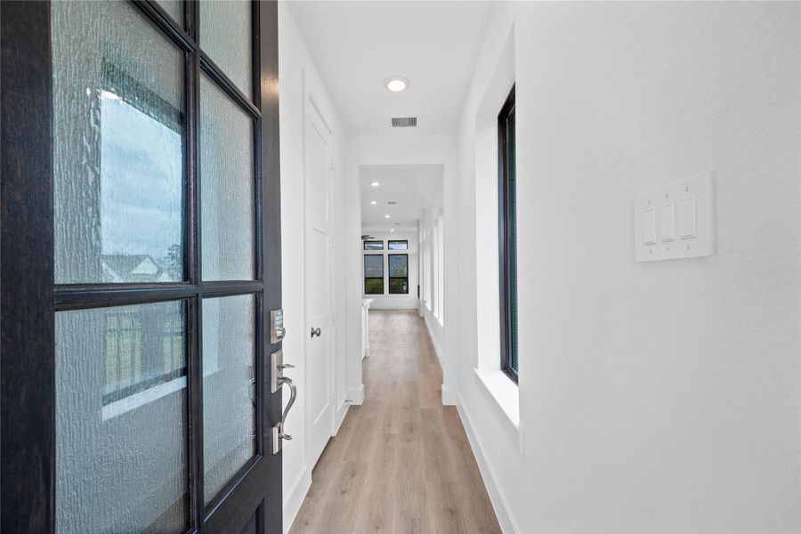 A bright and open interior entryway focuses on modern design and natural light. The space is amplified by high ceilings, recessed lighting, and generous natural light pouring in from large windows, creating an airy and welcoming first impression.