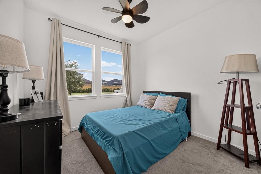 Cozy bedroom with large windows allowing natural light, neutral walls, and a modern ceiling fan, perfect for relaxation.