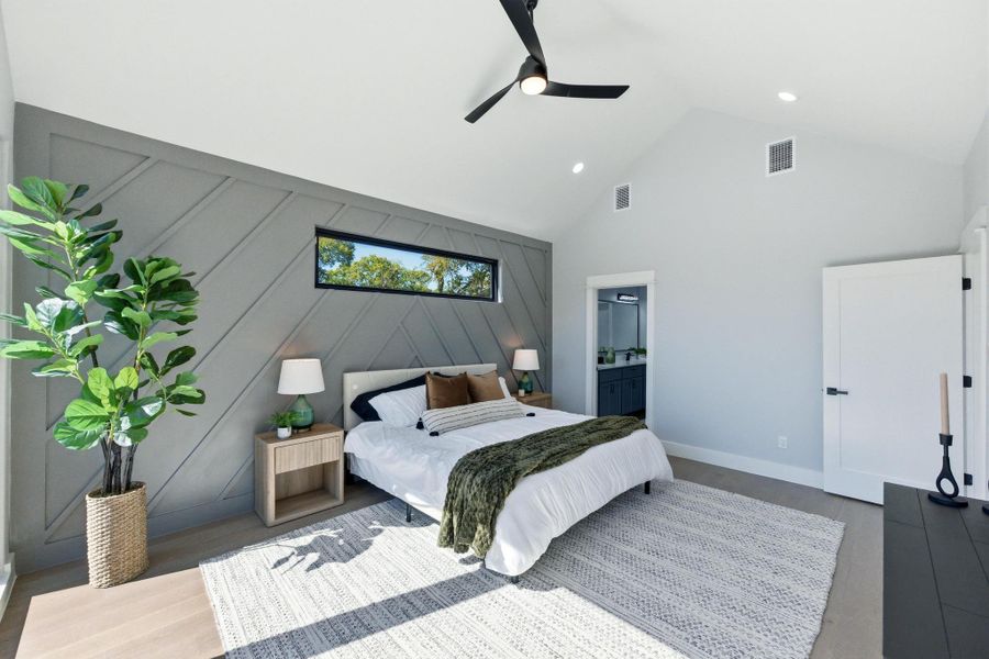 Bedroom with wood finished floors, high vaulted ceiling, connected bathroom, a ceiling fan, and a decorative wall Bedroom with wood finished floors, high vaulted ceiling, connected bathroom, a ceiling fan, and a decorative wall