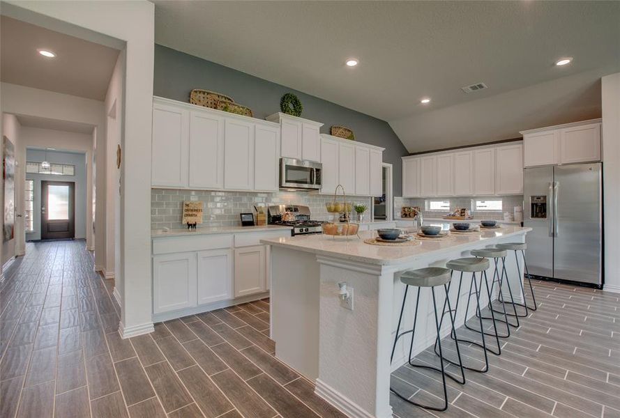 Kitchen featuring appliances with stainless steel finishes, tasteful backsplash, white cabinets, wood tiled floors, and recessed lighting Kitchen featuring appliances with stainless steel finishes, tasteful backsplash, white cabinets, wood tiled floors, and recessed lighting