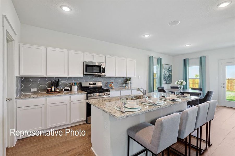 Open-concept kitchen featuring white cabinetry, stainless steel appliances, hexagon tile backsplash, granite countertops, and wood-finish flooring