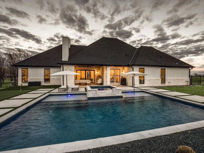 Rear view of house featuring a chimney, a patio area, a pool with connected hot tub, and stone siding