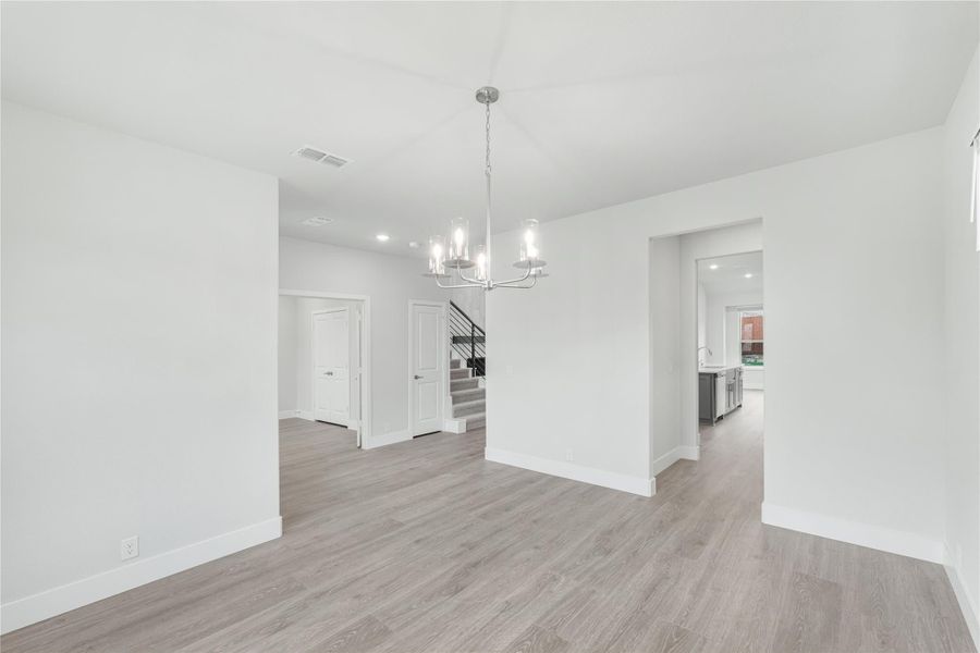 Open dining area with chandelier, light wood floors, white walls, and staircase visible in background