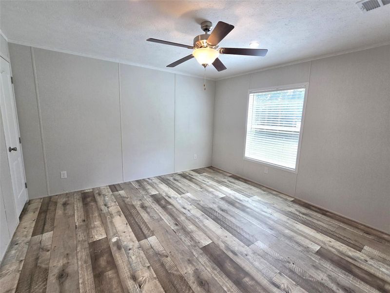 This inviting second bedroom boasts rustic wood-style flooring, ample natural light through a large window, and a modern ceiling fan, creating a cozy and stylish retreat. This inviting second bedroom boasts rustic wood-style flooring, ample natural light through a large window, and a modern ceiling fan, creating a cozy and stylish retreat.
