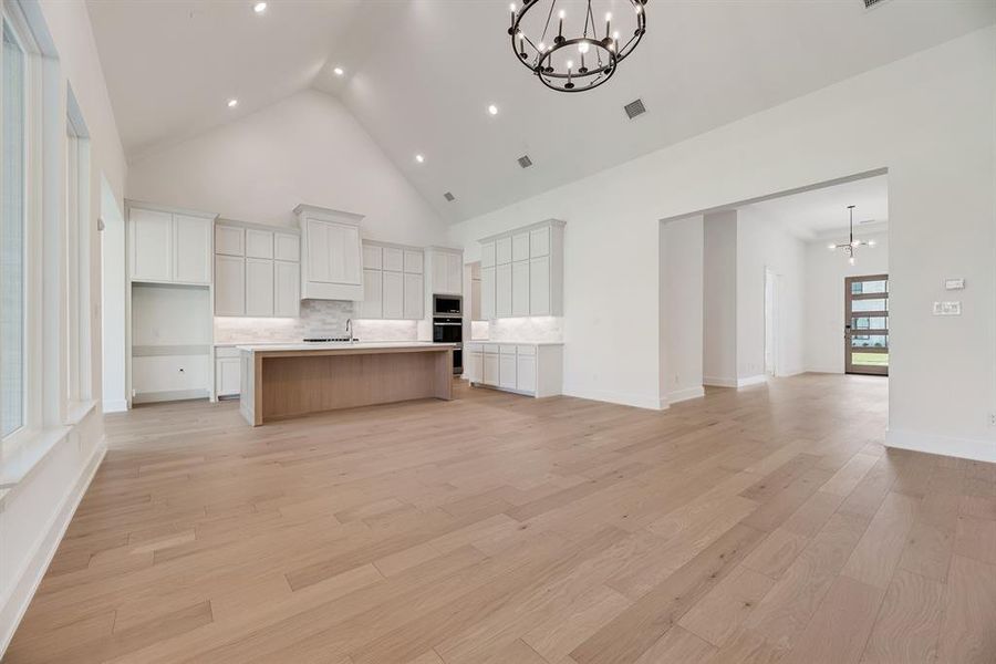 Kitchen featuring a chandelier, open floor plan, white cabinets, high vaulted ceiling, and a kitchen island with sink